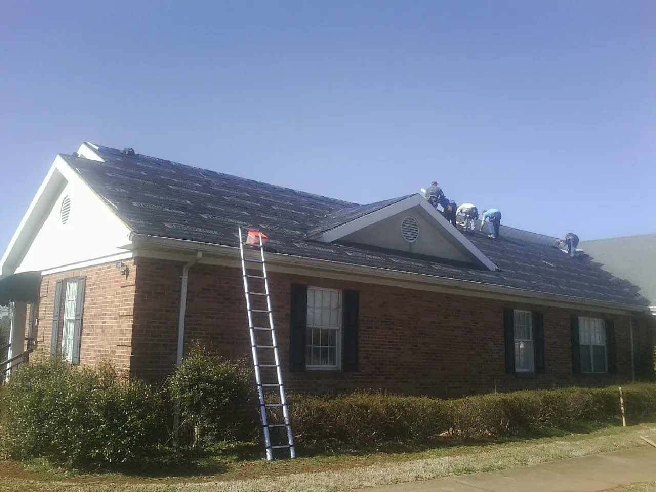 Crew tearing shingles off a brick ranch roof with a ladder set — Emergency Roof Repair work by our crew in Sharon