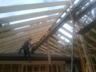 Rafters going up over a new addition with a worker on the wall in Sharon