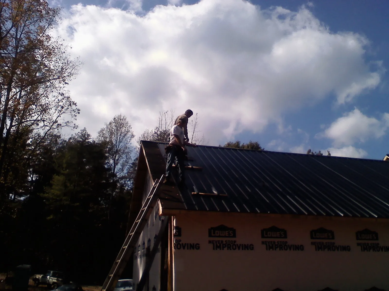 Roofer fastening dark metal panels high against a cloudy sky, from a Roof Inspection job in Sharon